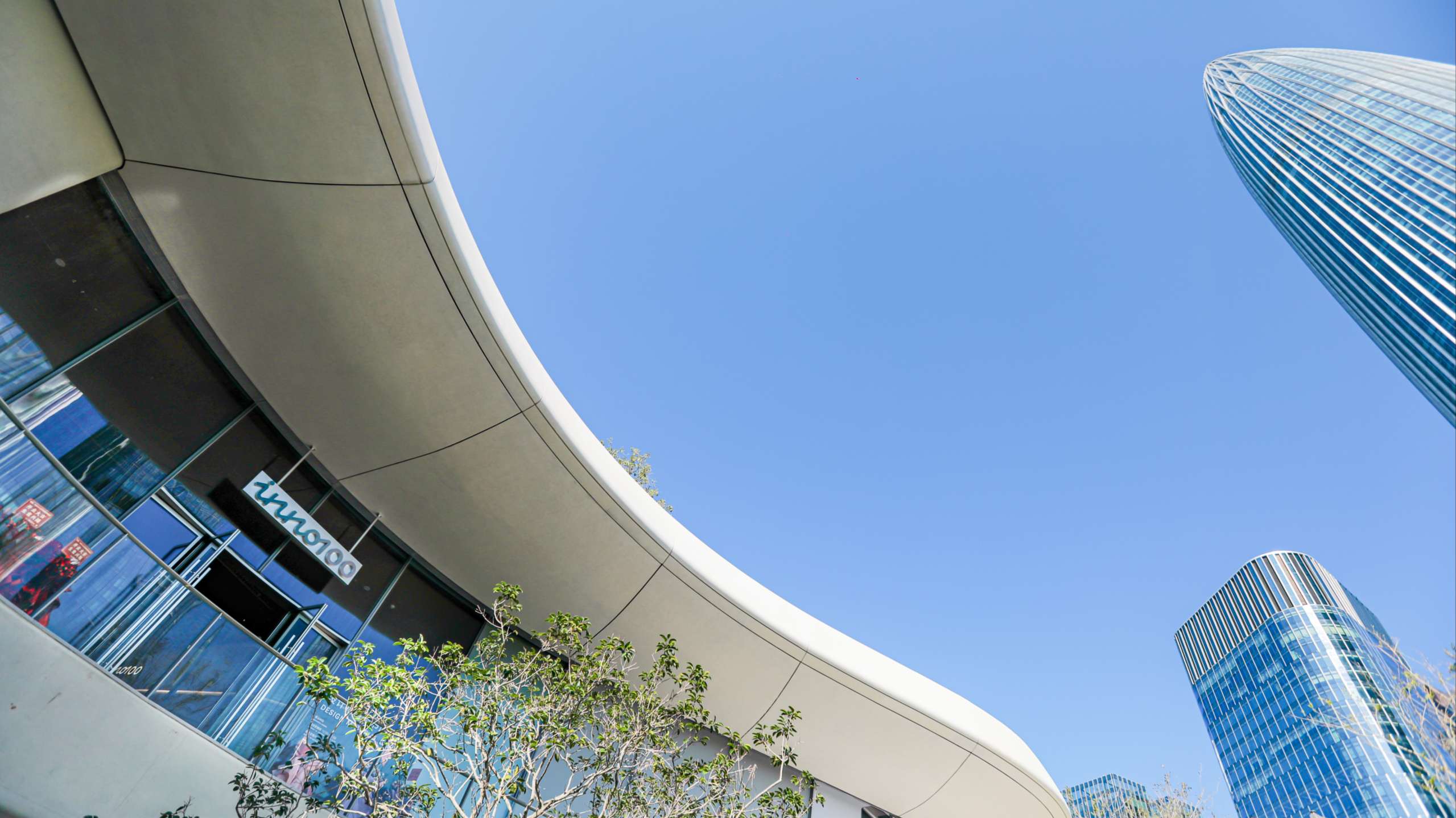 The curved exterior of the INNO100 flagship store featuring a modern glass facade and the brand logo under a clear blue sky in a high-tech district