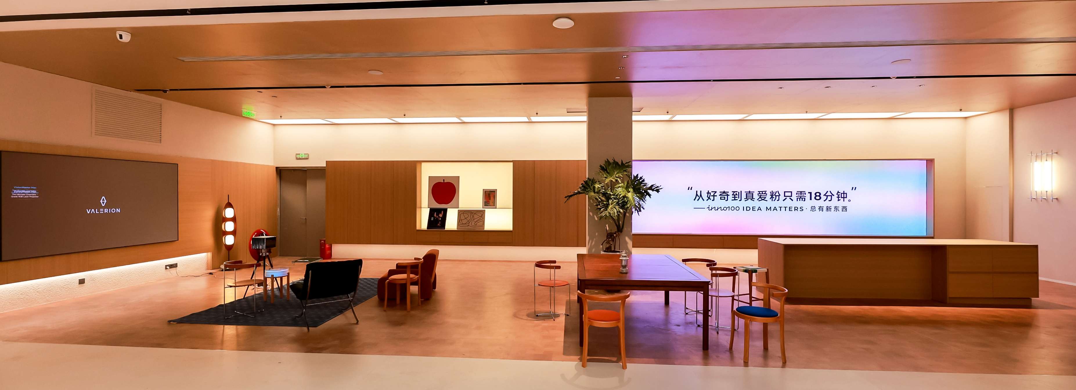 A modern, minimalist retail showroom featuring a lounge area with chairs, a central wooden table, and a large illuminated wall display with Chinese text